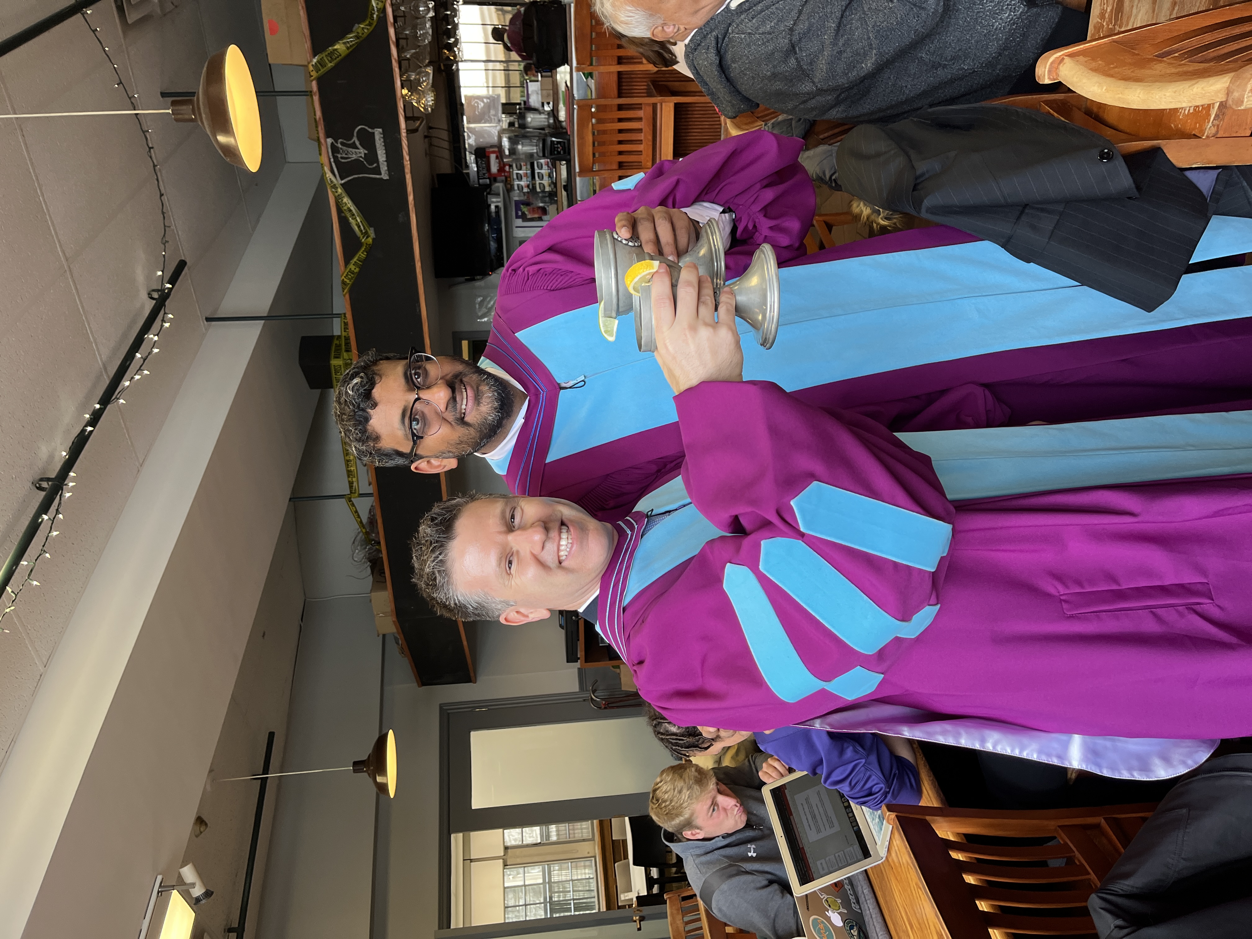 Two men in Graduation robes, drinking from the chalice of knowledge at the grad club